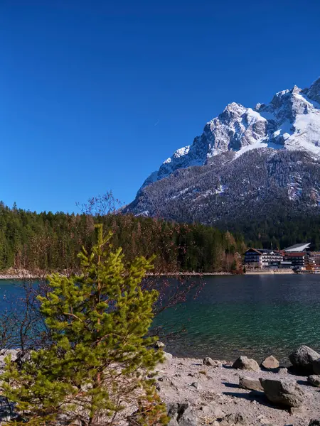 Sakin bir göl, aydınlık ve güneşli bir günde çevredeki dağları ve ormanı yansıtır. Çam ağaçları suların kenarında durur, doğal ortamın huzurlu atmosferini arttırır..