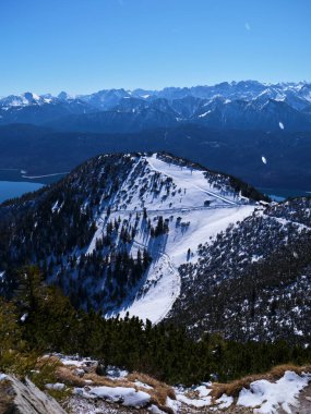 Görkemli karlı manzara, parlak mavi bir gökyüzünün altında sarmal bir patikayla çevrili bir dağ zirvesini yakalar. Huzurlu güzellik keşfi davet ediyor..
