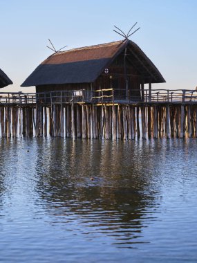 Ayaklıklar üzerinde kırsal ahşap kulübeler sakin bir gölün üzerinde duruyor. Titrek günbatımı durgun suya yansıyarak sakin bir atmosfer yaratıyor..