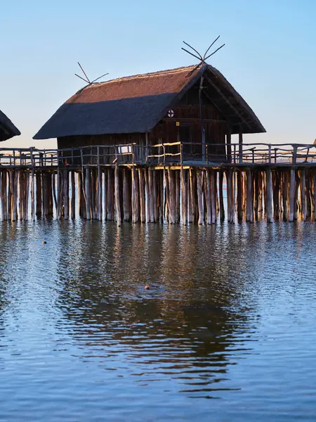 Ayaklıklar üzerinde kırsal ahşap kulübeler sakin bir gölün üzerinde duruyor. Titrek günbatımı durgun suya yansıyarak sakin bir atmosfer yaratıyor..