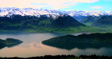 Görkemli dağlar dingin bir göl üzerinde yükselir, parlak mavi gökyüzünü ve yeşil vadileri yansıtır. Bu çarpıcı İsviçre manzarası güneş ışığı altında güzelliği sergiliyor..