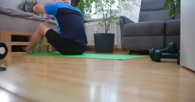 Bireyler, parlak ve havadar bir yaşam alanında yeşil bir paspas üzerinde çekirdek egzersizleri yaparlar. Bu çalışma konforlu bir ev ortamında sağlık ve refahı vurguluyor..