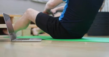 Yeşil bir paspasın üzerinde güç egzersizleriyle ev antrenmanı yapmak. Yakınlarda sanal rehberliği ya da eğitimi gösteren bir dizüstü bilgisayar var. Forma ve sağlığa odaklan..
