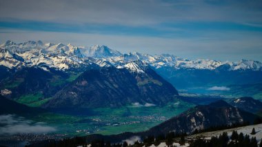 Karla kaplı zirveler canlı yeşil bir vadi üzerinde belirgin bir şekilde yükselir, açık bir günde İsviçre 'de nefes kesici bir doğa manzarası yaratır..