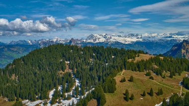 Yeşilliklerle kaplı yuvarlanan tepeler, göz kamaştırıcı kar örtülü dağ zirveleriyle çelişiyor, canlı mavi gökyüzünün altında, güzellikleri ve sükuneti sergiliyor..