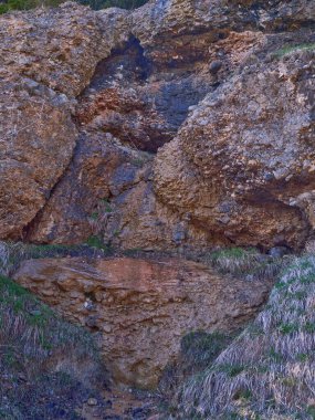 Yeşil çimenler ve açık gökyüzünün altındaki doğal bitki örtüsüyle çevrili su yüzeyinden yavaşça akarken eşsiz bir kaya oluşumu vurgulanır..