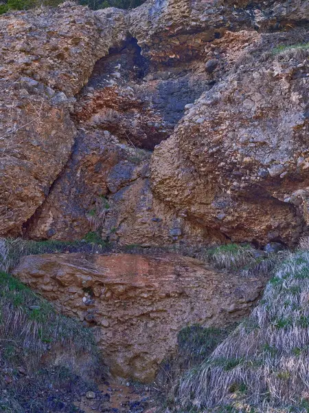 Yeşil çimenler ve açık gökyüzünün altındaki doğal bitki örtüsüyle çevrili su yüzeyinden yavaşça akarken eşsiz bir kaya oluşumu vurgulanır..
