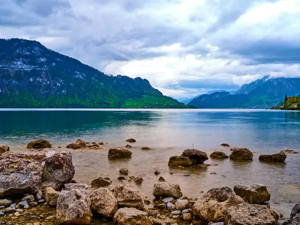 Sakin bir göl üzerimizdeki bulutları yansıtırken kayalık kıyılar ve yemyeşil dağlar sakin bir manzara yaratır. Atmosfer sakin ve resim gibi, rahatlatıcı..