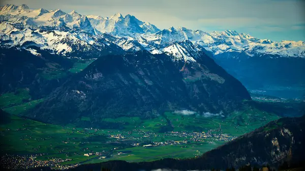 Karla kaplı görkemli tepeler İsviçre 'de parlak mavi bir gökyüzünün altındaki tuhaf köylerle kaplı yemyeşil vadilerin üzerinde. Nefes kesici bir manzara doğanın güzelliğini ortaya çıkarır..