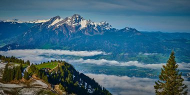 Kar kaplı İsviçre dağları güneş doğarken görkemli bir bulutlar denizi üzerinde, yemyeşil vadileri ve aşağıdaki küçük bir köyü gözler önüne seriyor, nefes kesici bir manzara yaratıyor..