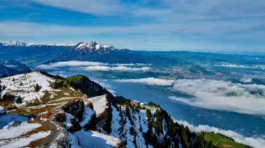 Karla kaplı dağlar sakin bir göl üzerinde güzel bir şekilde yükselirken, ince bulutlar altta yavaşça süzülüyor, açık bir günde nefes kesici bir dağ manzarası yaratıyor..