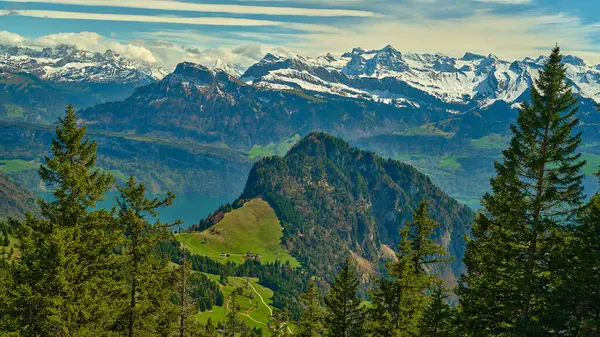 Yükselen karlı dağların altında yemyeşil tepeler yükseliyor. Uzakta görülen safir bir göl var. Bu dağlık bölgenin dingin güzelliğine berrak bir gökyüzü katar..