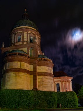 Aydınlık bir ayın aydınlattığı karanlık bir gökyüzüne karşı belirgin bir tarihi yapı vardır. İnce bulutlar huzur dolu geceye atmosfer katıyor..