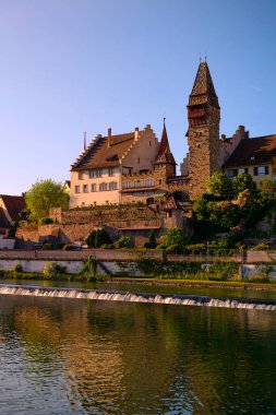Bir ortaçağ şatosu sakin bir nehrin kıyısında günbatımının ılık renklerini yansıtan görkemli bir şekilde duruyor. Yeşillik tarihi bölgeyi çevreleyerek, Avrupa 'da sakin bir atmosfer yaratıyor..