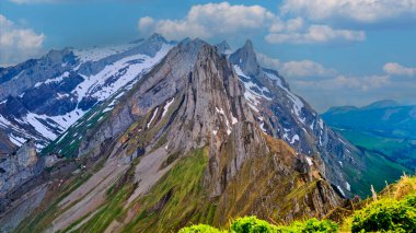 Bereketli yeşil battaniyeler dik dağ yamaçları gibi engebeli tepeler berrak mavi gökyüzüne karşı kule gibi. Karla kaplı zirveler, dağlık alanda ipuçları verir. Huzurlu ve nefes kesici bir manzara doğada belirir..