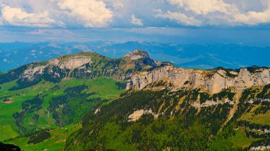 Görkemli dağlar dramatik bulutların zeminine karşı yükseliyor, kayalık kayalıklar ve yeşil vadiler sergiliyor. Doğa canlı tonlarda ortaya çıkar ve dingin bir şekilde genişler..