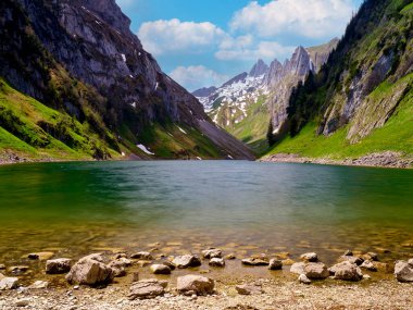 Dağ gölünün berrak suları etrafındaki kayalık tepeleri ve yemyeşil tepeleri yansıtıyor. Güneşli bir günde İsviçre Alplerinin dingin güzelliğini gösteriyor..