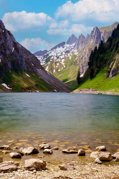 Dik dağ kayalıklarının arasına kurulmuş sakin bir alp gölü nefes kesici bir manzara. Karla kaplı zirveler parlak mavi gökyüzünün altındaki berrak suları yansıtarak sakin bir manzara yaratır..