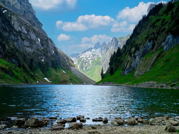 Sakin bir göl dik dağ yamaçlarının arasına kurulmuş, yemyeşil ve kayalık çıkıntılar sergiliyor. Ayar yumuşak bulutlu parlak mavi bir gökyüzüne sahip, dingin atmosfere ekleniyor..