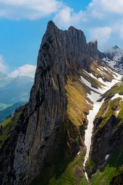 Bereketli vadilerin ve kar yığınlarının üzerinde çarpıcı bir dağ zirvesi, güneşli bir yaz gününde açık mavi gökyüzünün altında doğanın güzelliğini gözler önüne seriyor..