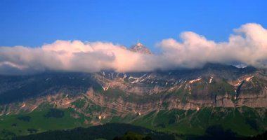 Görkemli dağlar dramatik bir şekilde yükselir, tepeleri dalgalı bulutlarla kaplanırken yemyeşil vadiler aşağıda uzanır, İsviçre 'nin doğal güzelliklerini gözler önüne serer..