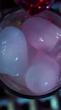 Sıvı dolu bir bardakta renkli buz küpleri parlıyor ve sosyal bir toplantı için canlı bir hava yaratıyor. Işıklandırma görsel cazibeyi arttırır, zevki davet eder..