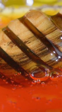 Bal, kalın tutarlılığını ve zengin rengini gösteren ahşap bir kepçeden yavaşça akar. Arkaplan kabarcıklar ve parlak renkler içererek, çekici sunumu geliştirir.