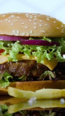 Marul, domates, soğan ve peynirle dolu lezzetli bir hamburger ahşap bir masada duruyor. Kızarmış patatesler bu ağız sulandıran yemeğe eşlik ediyor, öğle yemeği için mükemmel..