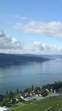 Sakin bir göl mavi gökyüzünü ve arkasında yeşil tepeler bulunan tüylü bulutları yansıtır. Küçük tekneler suda yavaşça hareket eder, sakin manzarayı güçlendirir..