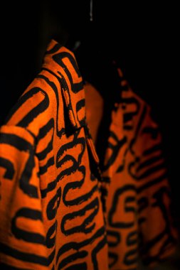 Tarz sahibi turuncu bir tişörtün detaylı bir yan görüntüsü. Geometrik siyah çizgiler desenli. Siyah bir arkaplanda asılı duruyor. Giysi detaylarını çevrimiçi perakende veya moda bloglarında göstermek için harika.