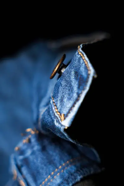 Siyah bir arka planda izole edilmiş, tasarımıyla ve işçiliğiyle ilgili, bir kot pantolonun üzerindeki düğmenin detaylı yakın plan çekimi. Moda pazarlama ve ürün kataloglarında detayları vurgulamak için harika..