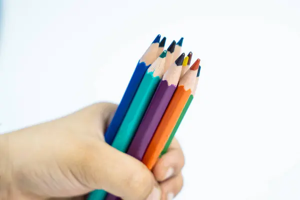 Elinde renkli kalemler tutan bir çocuğun, beyaz arka planda eğlenceli bir sanat aktivitesi için hazır olduğu eğlenceli bir fotoğraf. Ebeveynlik ve okulla ilgili içerik için mükemmel.