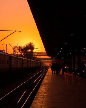 Alacakaranlığın güzelliği, sonsuz yolculukların sembolü olan demiryolu hatlarında yakalanır. İnsanlar tren istasyonunda bekliyor..