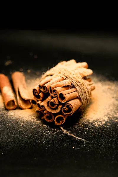 Yemek fotoğrafçılığı, tatil promosyonları ve yaşam tarzı blogları için siyah ideale izole edilmiş tamamlayıcı baharatlar ve doğal elementlerle çevrili tarçın çubuklarının güzel bir şekilde biçimlendirilmiş görüntüsü..