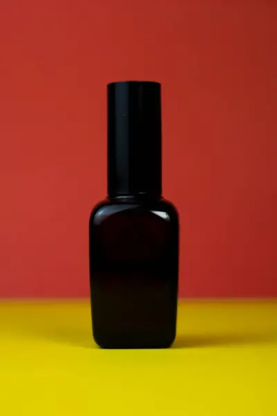 Kırmızı zemin üzerinde zarif bir siyah cam saç serumu şişesi. Lüks saç bakım ürünleri sunumları için mükemmel.