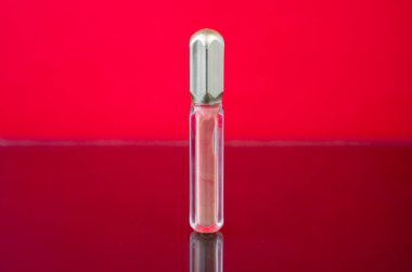 Kırmızı arkaplanda hafif şeftali rengi dudak parlatıcısı, kozmetik reklamlar ve ürün gösterimleri için ideal