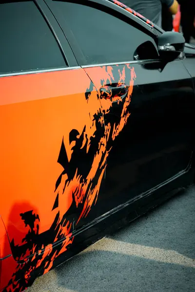 Turuncu ve siyah renkli şık bir spor araba, hız ve tavırları vurgulayan göz alıcı grafik çıkartmalarla süslenmiş. Otomotiv meraklıları için ideal