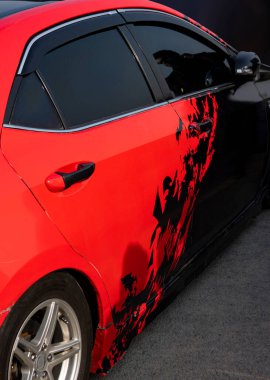Çarpıcı kırmızı ve siyah bir araba yan tarafları boyunca canlı sticker tasarımlar içeriyor, kişiselleştirmenin ve sokak stili yeteneğin bir karışımını vurguluyor. Modifiye edilmiş araçları göstermek için mükemmel