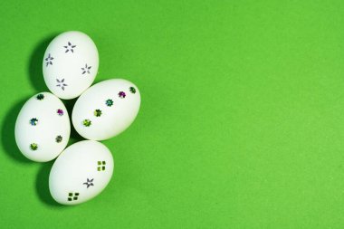 Canlı yeşil kağıdın üzerinde parlak süslemeleri olan beyaz yumurtalar Paskalya temalı tasarımlar ve mevsimsel pazarlama için mükemmel..