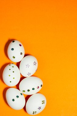 Renkli süslemelerle süslenmiş beyaz yumurtalı minimalist Paskalya konsepti, temiz ve modern bir festival görüntüsü için koyu turuncu bir zemin üzerine yerleştirilmiş..