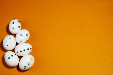 Turuncu bir zemin üzerine yerleştirilmiş çiçek ve geometrik pullarla süslenmiş beyaz yumurtalar, afişler, kartlar, reklamlar veya mevsimsel pazarlama için idealdir.