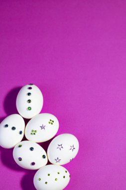  Açık Mor Arkaplanda Dekoratif Beyaz Yumurtalarla Düz Yerde. Düz bir düzende el yapımı yumurta süslemeleri ile modern festival tasarımı, Paskalya reklamları, kartlar ve promosyonlar için mükemmel.