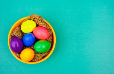 Mavi Arkaplanda Kırsal Bowl 'da Çoklu Renkli Yumurtalarla Paskalya Düz Yatağı. Dekoratif iplikle döşenmiş desenli bir kasenin içine yerleştirilmiş renkli yumurtaların en iyi görüntü fotoğrafı..