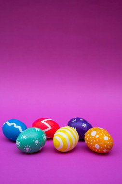 Değişik desenlerle süslenmiş canlı Paskalya yumurtaları, neşeli bir hava için pastel pembe bir yüzey üzerinde şekillendirilmiş..