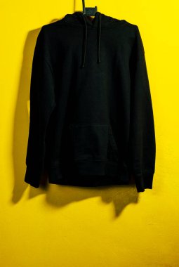 Gündelik siyah kapüşonlu parlak sarı arka planda asılı, modern ve şık moda gösterileri için mükemmel bir kontrast vurguluyor..