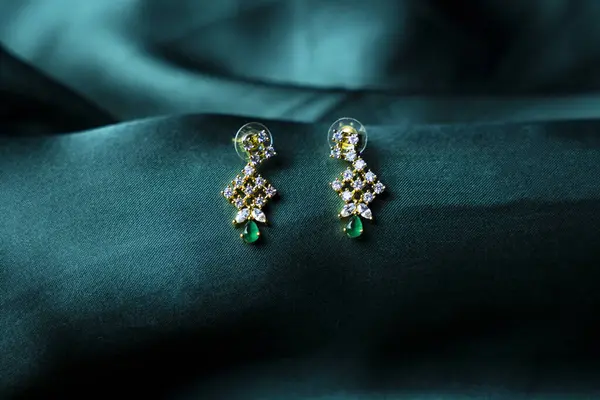 Yeşil pürüzsüz kumaşa takılmış incili bir çift güzel altın küpe..