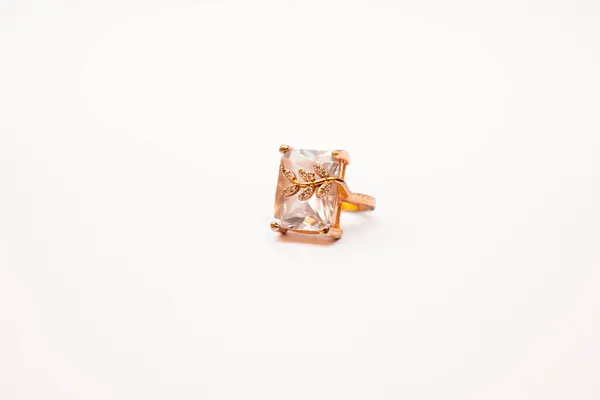 Bu resim, temiz beyaz bir arkaplanda duran güzel işlenmiş bir gül altın yüzüğünü gösteriyor. Yüzük, dört pençe ile korunan ve taşın üzerine ince bir altın yaprak dizaynı yerleştirilmiş, belirgin, şeffaf bir mücevher sergiliyor.. 