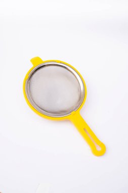 Minimalist yemek fotoğrafçılığı. Beyaz arka planda sarı plastik bir ağ çay süzgeci.
