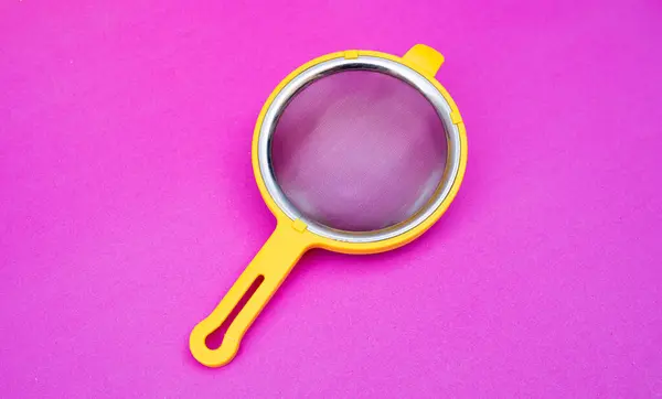 Sarı çay ya da ince örgülü mutfak süzgeci parlak pembe bir arka plana yerleştirilmiş, yukarıdan izole edilmiş ve çekilmiş..