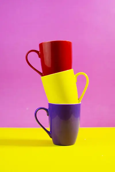 Parlak çok renkli seramik bardaklar canlı pembe ve sarı stüdyo arkaplanlarına karşı dikey olarak dizilmiş.